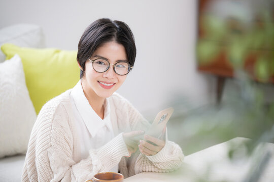 Woman wearing knitwear, tapping her smartphone, looking at a shortcut Close-up with green foreground blur