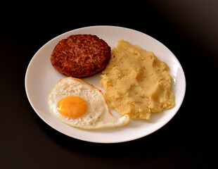 Fried chicken egg, mashed potatoes and juicy beefsteak in a round plate on a black background.