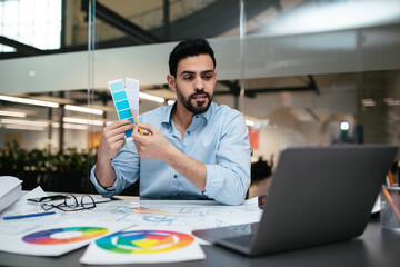 A man is actively engaged in a design meeting, showcasing color swatches while seated at a desk.