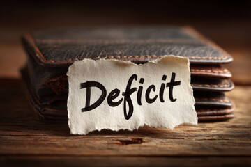 A torn paper with the word “Deficit” placed inside a brown leather wallet, symbolizing personal finance issues, money shortage, and budget deficit.