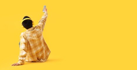 Man with TV remote controller and headphones sitting on yellow background with space for text, back...