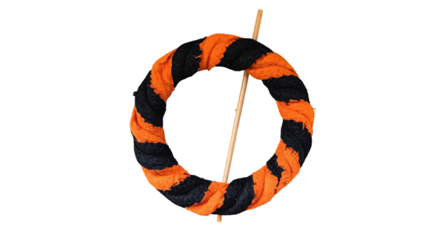 Wreath-like object with alternating orange and black twisted fabric, skewered by a wooden stick on a black backdrop