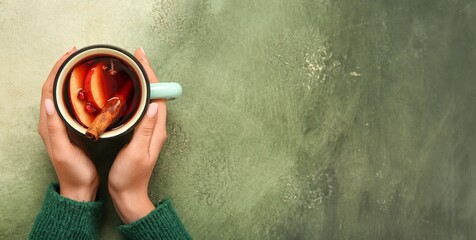 Woman's hands holding cup of hot mulled wine on green background with space for text, top view