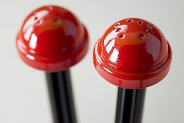 Two shiny red salt & pepper shakers with holes on white seamless background