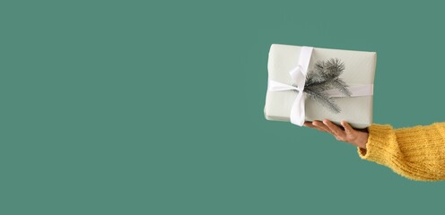 Female hand with Christmas gift on green background with space for text