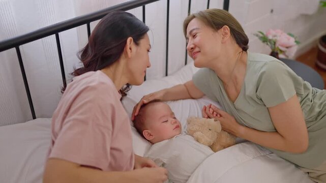 Asian lesbian couple lovingly caring for and raising their baby boy at home. 