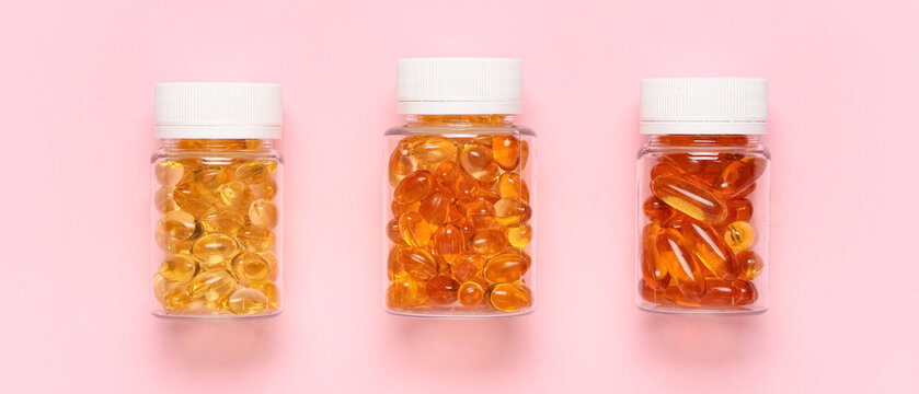 Jars with vitamin E capsules on pink background, top view