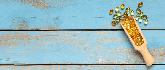 Scoop with vitamin E capsules on blue wooden background with space for text, top view