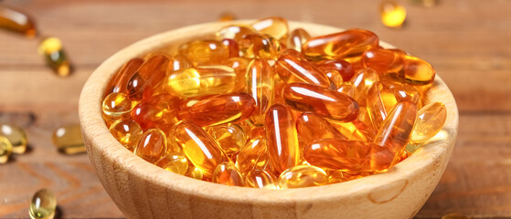 Bowl with vitamin E capsules on wooden background, closeup