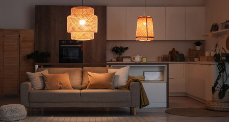 Interior of kitchen with counters, sofa and glowing lamps at night