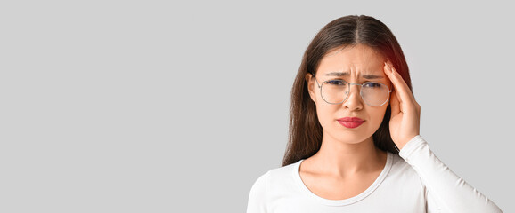 Young Asian woman suffering from headache on grey background. Brain Injury Awareness Month