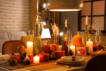 Festive table setting with burning candles, pumpkins and greeting cards for Thanksgiving Day at evening