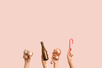 Female hands holding Christmas balls, candy cane and bottle of champagne on pink background