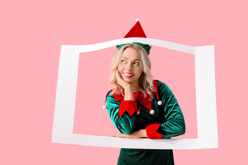 Thoughtful young woman dressed as elf with frame on pink background