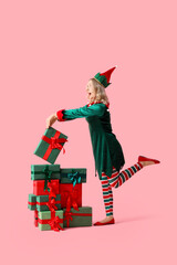 Happy young woman dressed as elf with Christmas gifts on pink background