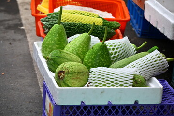 Green melons in white foam box with mesh protection, orange basket with yellow-netted melons behind, blue plastic basket base, outdoor gray pavement, market produce display, Taiwan.