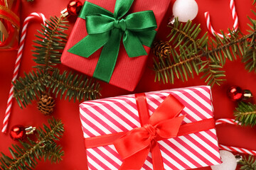Christmas gift boxes with balls, fir tree branches and candy cane toys on red background