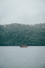 Tour boat sailing on calm water near a tropical forest on a cloudy day, Koh Kood, Trat, Thailand