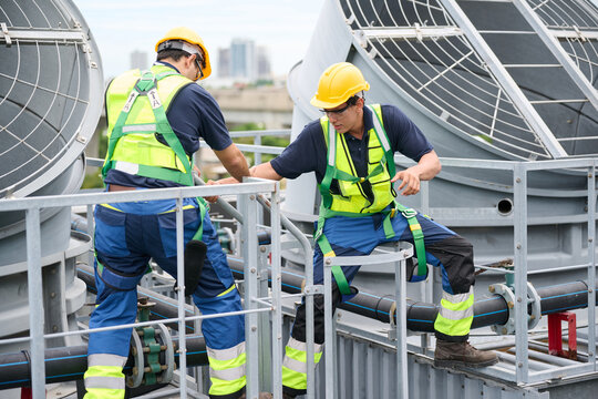 Construction workers collaborating on a rooftop, emphasizing safety and teamwork in an industrial setting. They are wearing safety helmets and harnesses