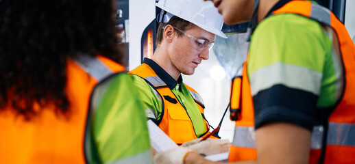 Industrial workers wearing safety gear are discussing project plans and reviewing technical documents on the modern factory manufacturing. Teamwork collaboration on construction site