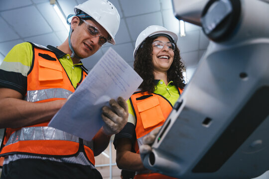 Experienced engineer in safety gear collaborating to operate and inspect a high-tech CNC machine and check technical documents on the production factory. Teamwork at automation industry