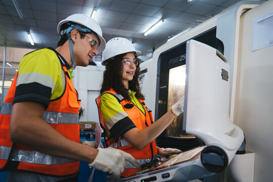 Industrial engineers in safety gear are discussing the production process while operating a modern CNC machine and checking its control panel in a manufacturing factory. Teamwork collaboration - Powered by Adobe