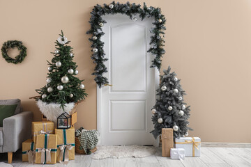 White door with fir branch, decorated Christmas trees and gift boxes near color wall at home