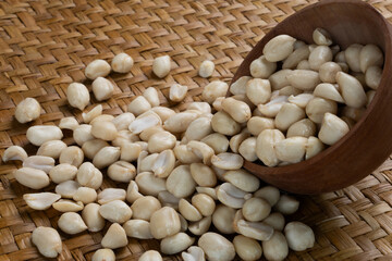 Close-up of Raw Shelled Peanuts Spilling from a Wooden Scoop onto a Brown Woven Mat