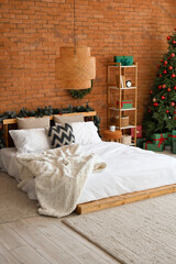 Interior of bedroom with Christmas tree, gifts and decor near orange brick wall