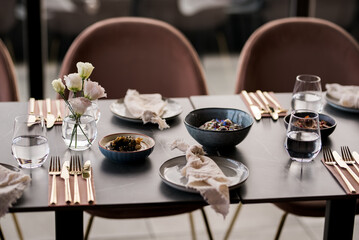 A beautifully set modern dining table with elegant tableware, delicate flowers, and soft natural light — ready for guests to enjoy a stylish meal together.