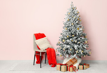 Decorated Christmas tree with gift boxes, chair and sack near pink wall