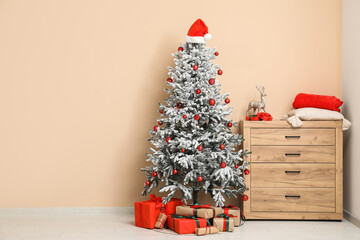Decorated Christmas tree with gifts and chest of drawers with deer, gifts, cushion and plaid in interior of living room