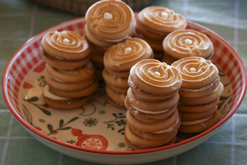 Appetizing homemade butter cookie stacks on decorative plate. This delicious sweet dessert, swirl biscuit snack, makes comforting and tasty treat on checkered tablecloth