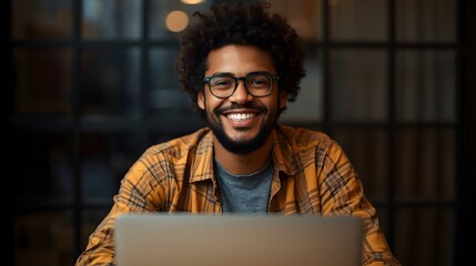 Confident young man wearing glasses smiling while working on a laptop in a modern office or café, representing remote work, freelance lifestyle, creativity, technology, and professional success