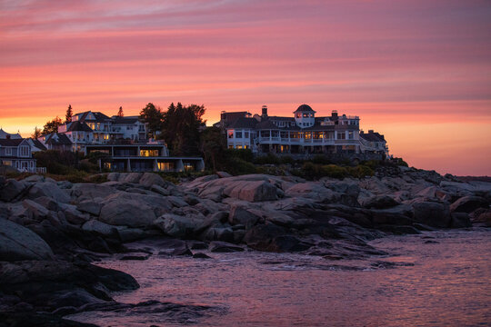 Sunset view over the rocky coastline of ogunquit, maine, with elegant oceanfront homes glowing in warm evening light. soft pink and orange sky creates a peaceful coastal atmosphere.