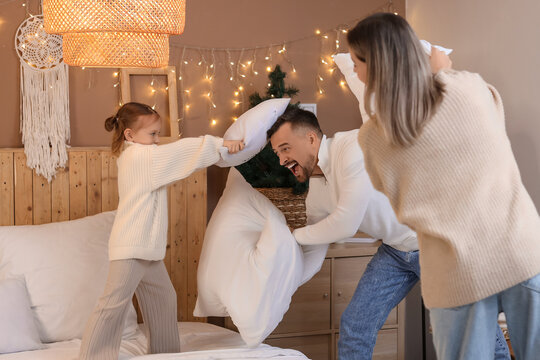 Happy parents and their little daughter fighting pillows in winter evening at home