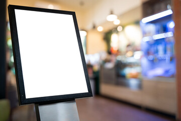 Blank white poster frame stand in front of blurred cafe interior background for advertising or...