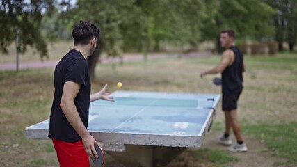 Friends are actively playing table tennis outdoors in a park, enjoying their recreational time together. This scene captures their spirited game and the healthy, fun atmosphere of friendship and sport