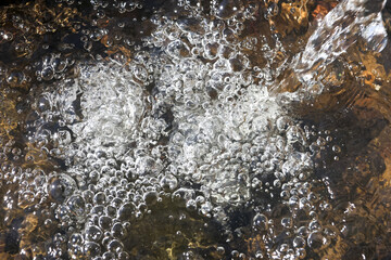 Bubbling clear water flowing over rocks in shallow stream creates refreshing and energetic natural background. sparkling surface shows pure, dynamic movement of liquid
