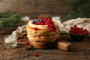 Plate of sweet pancakes with berries burning candles and Christmas tree branches on wooden background