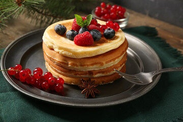 Plate of sweet pancakes with berries and Christmas tree branch on wooden table