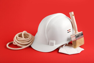 White hardhat with brush, rope and protective face mask on red background