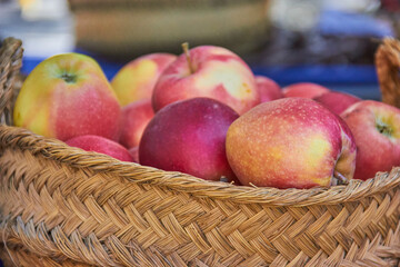 Fresh apples with red and yellow skin displayed in a rustic woven basket at a local Granada market in Spain, highlighting seasonal produce. autumn fruit