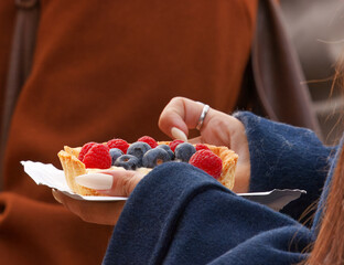 A young woman holding holding a fresh berry tartlet at the Naplavka Farmers Market in Prague.