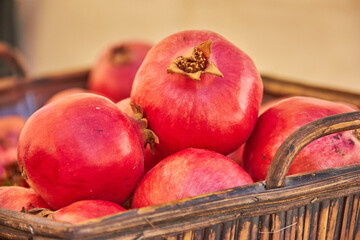 A wooden basket filled with ripe red pomegranates on display at a market in Granada, Spain, glowing in the warm sunlight. freshness harvest