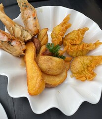 A beautifully presented platter  of golden brown fried appetizers arranged on a scallop - edged white dish. 