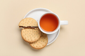 Plate with tasty sandwich biscuits and cup of tea on beige background