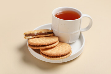 Plate with tasty sandwich biscuits and cup of tea on beige background