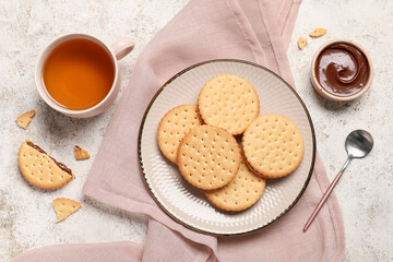 Plate with tasty sandwich biscuits, chocolate cream and cup of tea on light grunge background