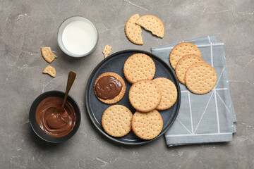 Plate with tasty sandwich biscuits, chocolate cream and glass of milk on grey grunge background